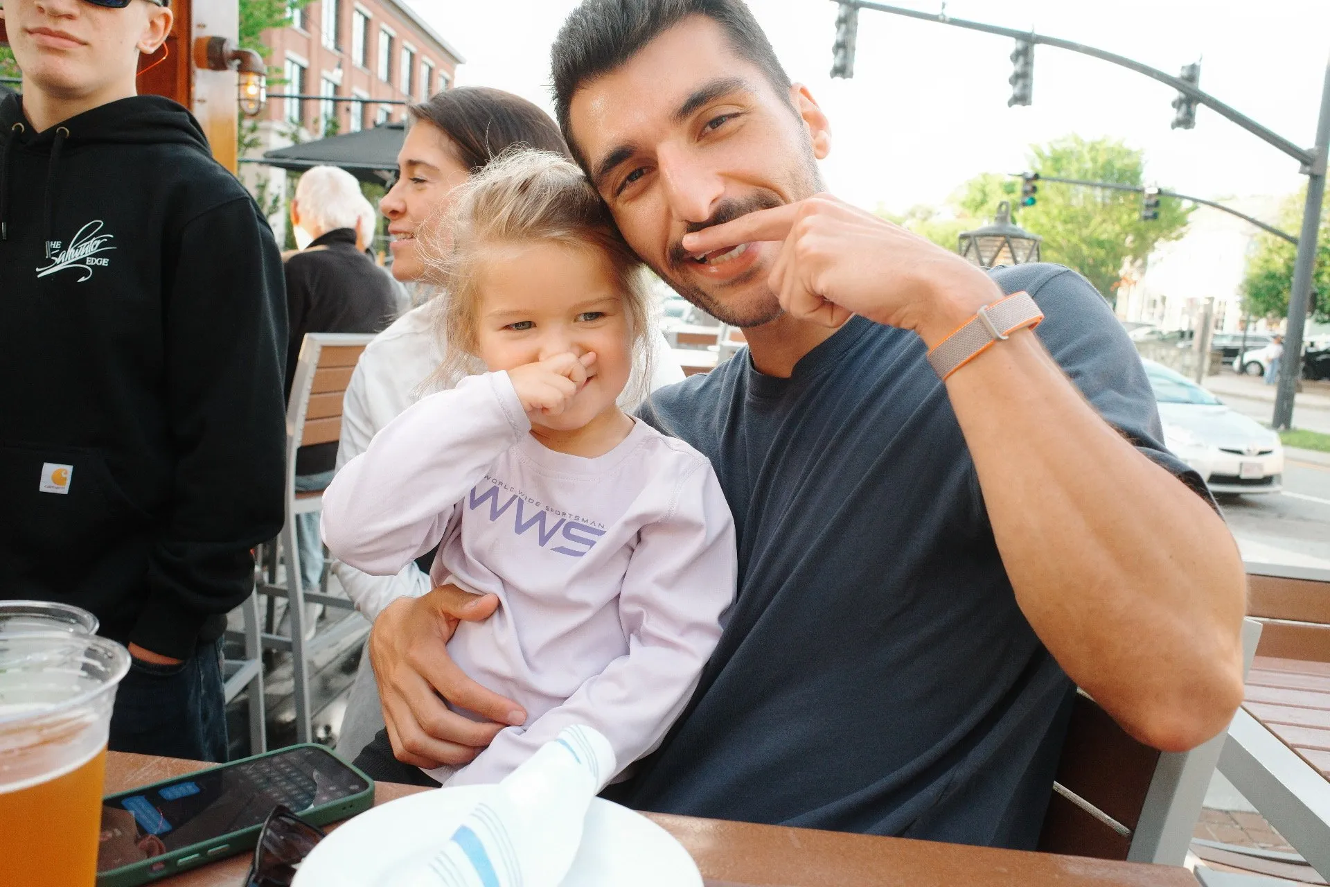 Alex at an outdoor table with a little girl, both touching their noses